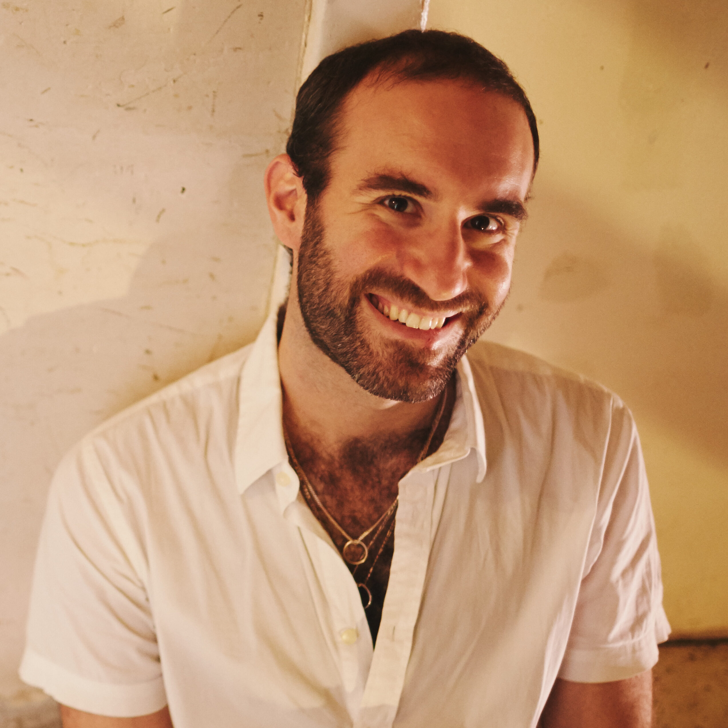Young man leaning against a wall smiling.